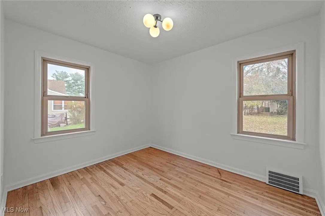 Empty room with light wood-style floors, plenty of natural light, and a textured ceiling