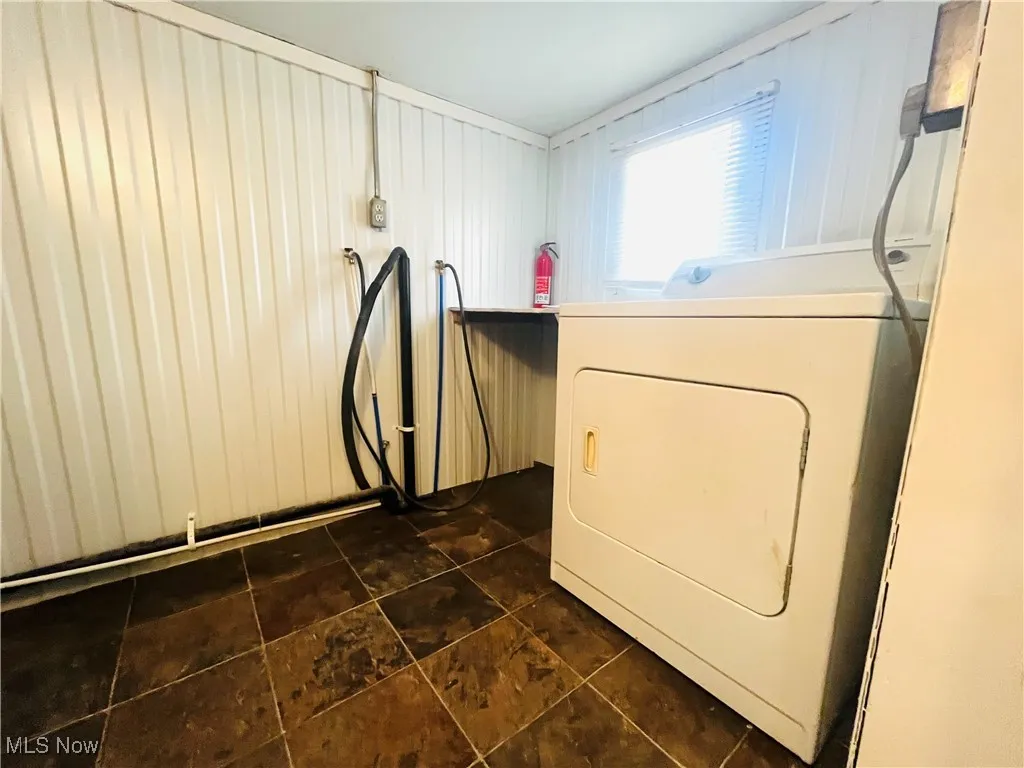 Laundry room with washer / dryer, wooden walls, and dark tile patterned floors