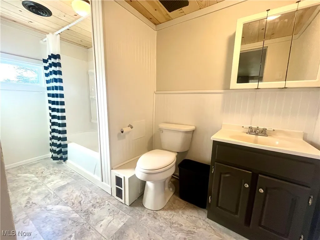 Bathroom with wooden ceiling, vanity, shower / bath combo, and wainscoting