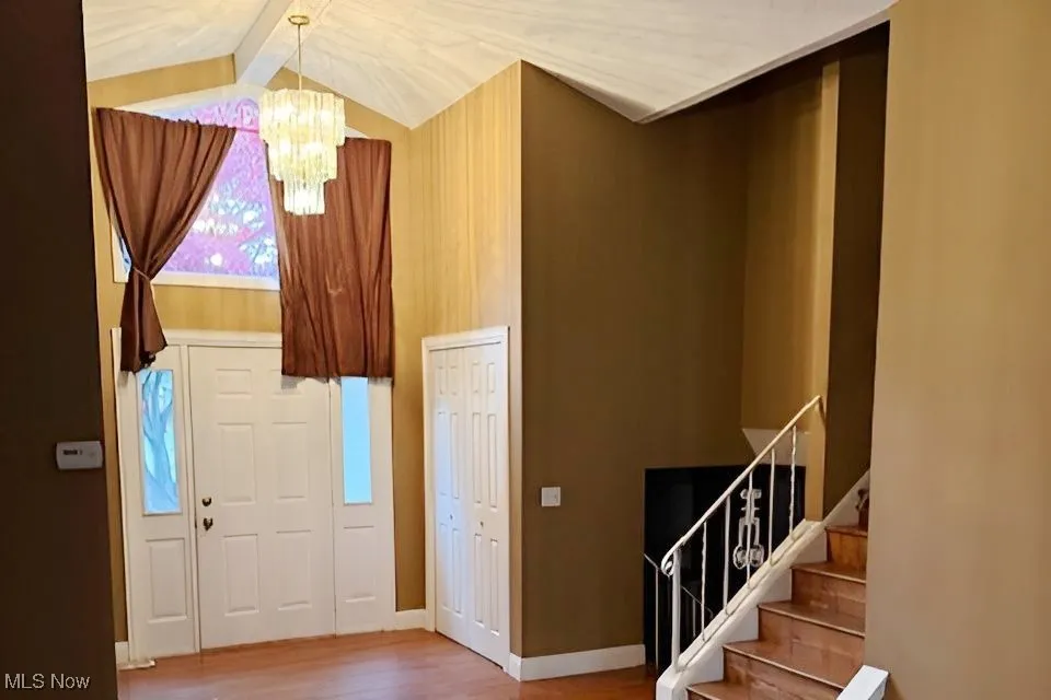 Foyer entrance with a chandelier, light wood-style floors, high vaulted ceiling, beamed ceiling, and stairs
