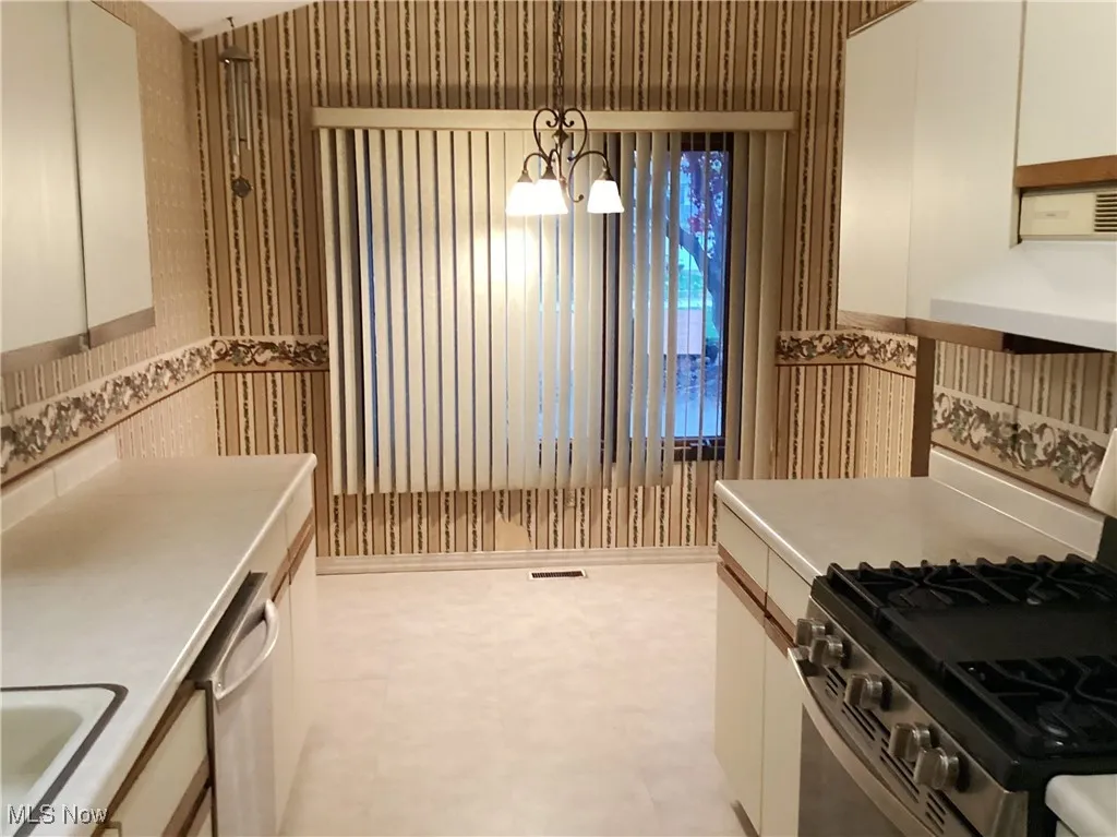Kitchen with stainless steel appliances, light countertops, under cabinet range hood, decorative light fixtures, and white cabinetry