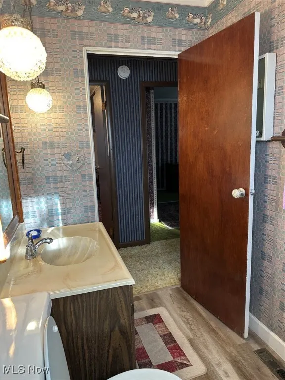 Bathroom featuring wallpapered walls, LVF flooring, and vanity