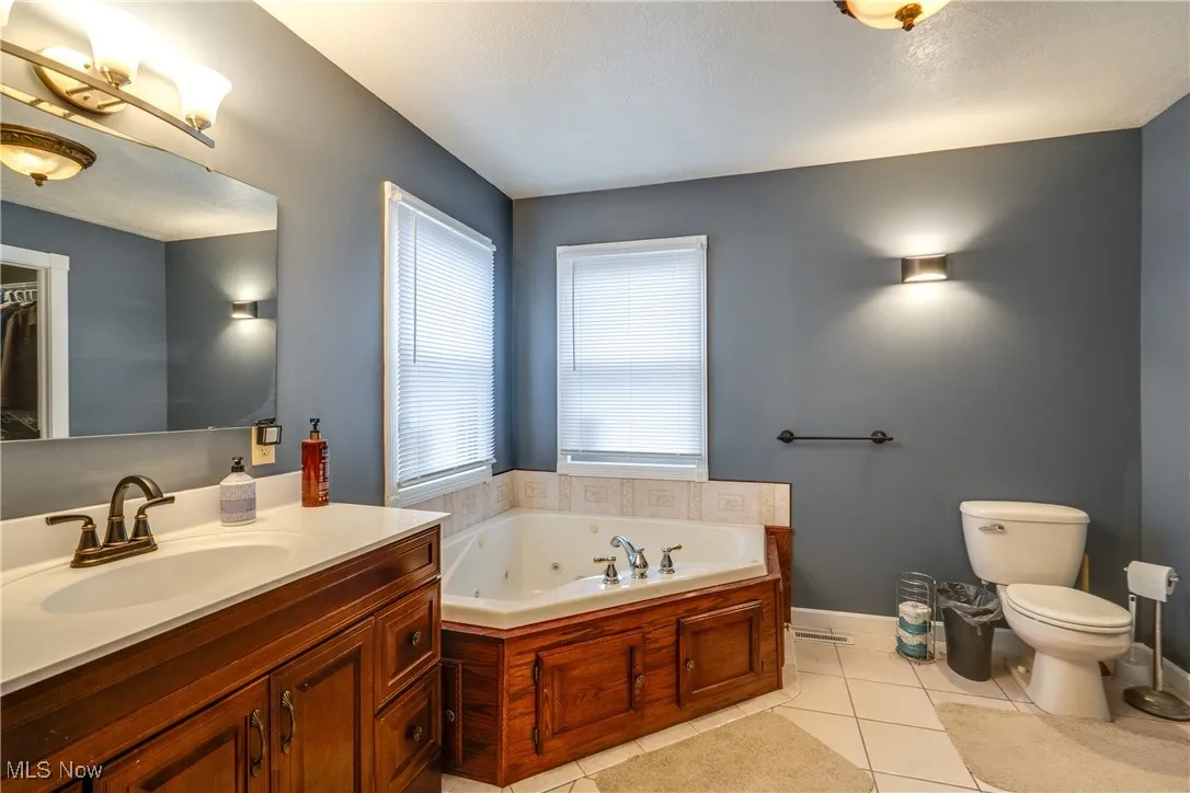 Bathroom with light tile patterned flooring, a whirlpool tub, vanity, and a textured ceiling