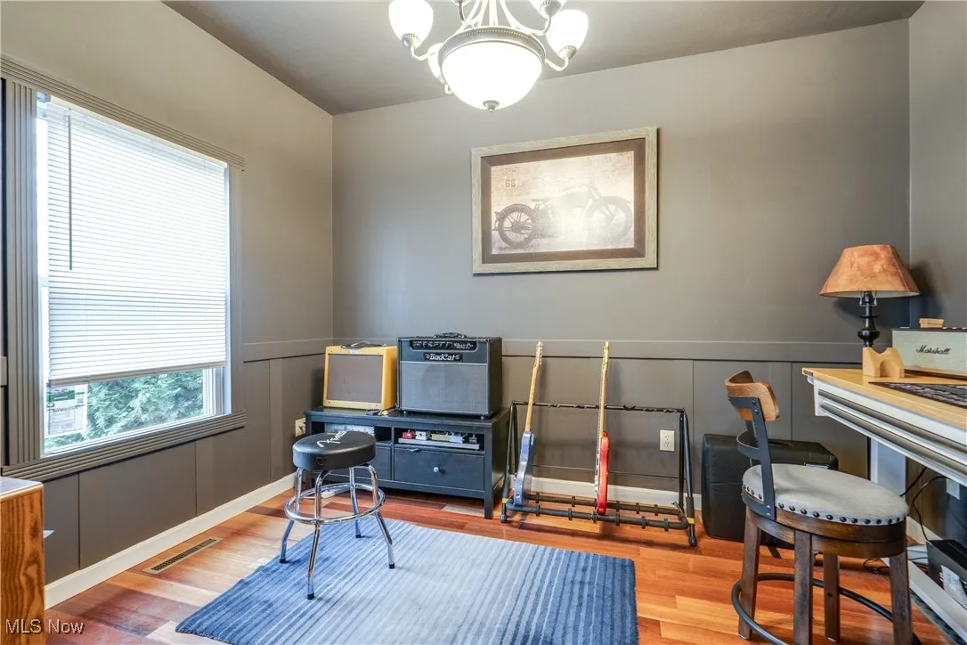 Home office with healthy amount of natural light, a chandelier, wood finished floors, a decorative wall, and wainscoting