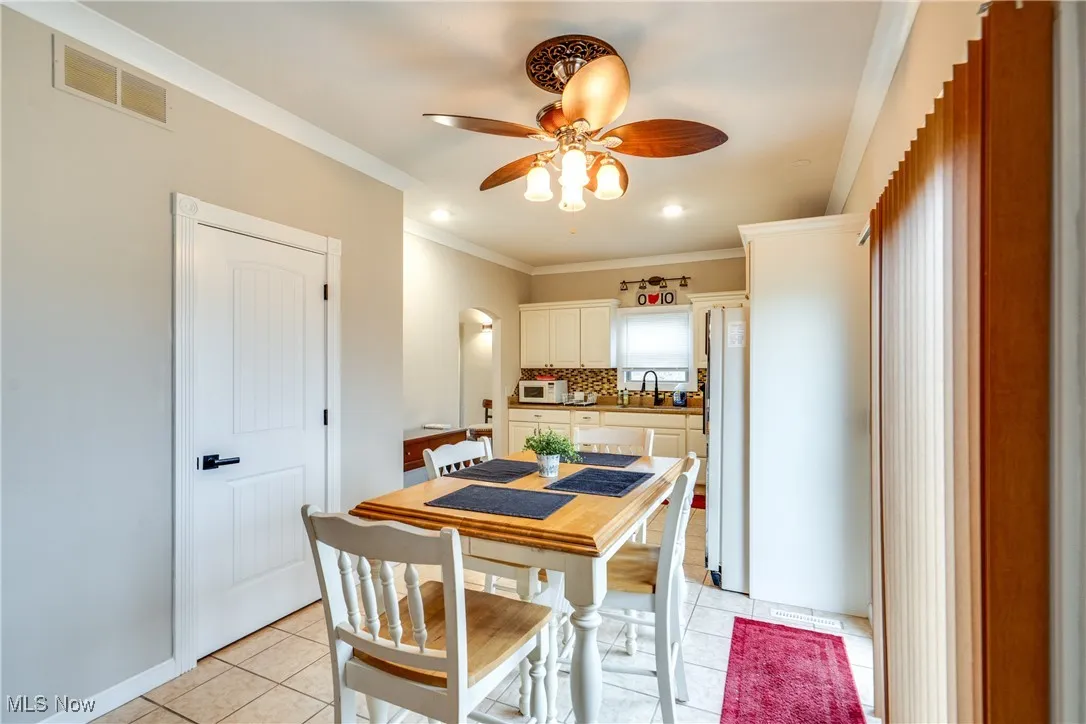 Dining room featuring ceiling fan, ornamental molding, arched walkways, and light tile patterned flooring