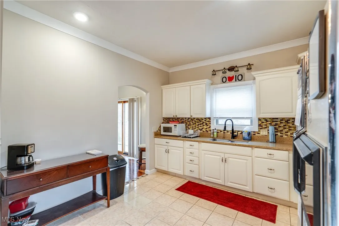 Kitchen with arched walkways, tasteful backsplash, ornamental molding, white microwave, and white cabinetry