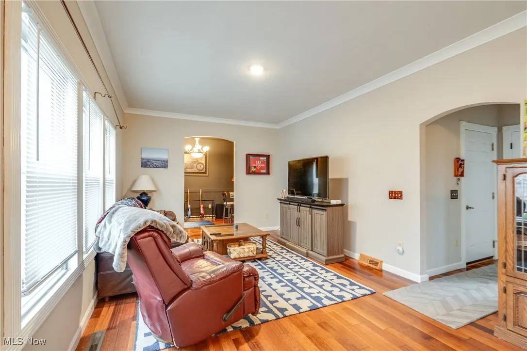 Living room featuring arched walkways, ornamental molding, wood finished floors, and a chandelier