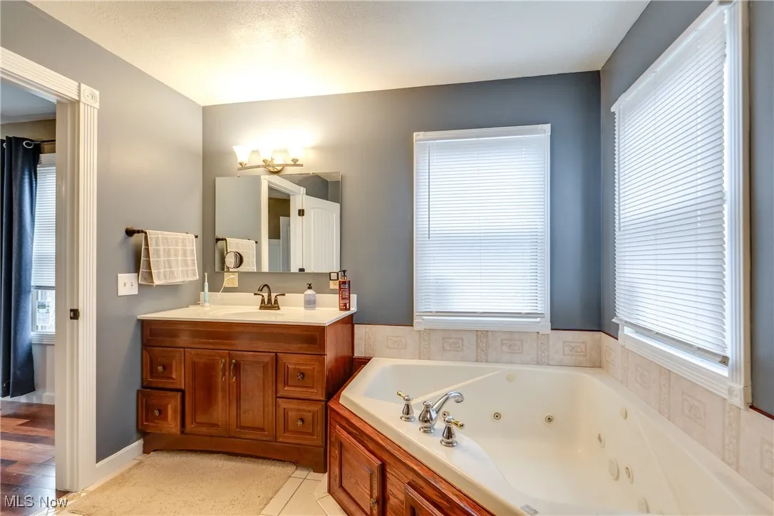 Bathroom featuring a whirlpool tub, vanity, plenty of natural light, and light tile patterned floors