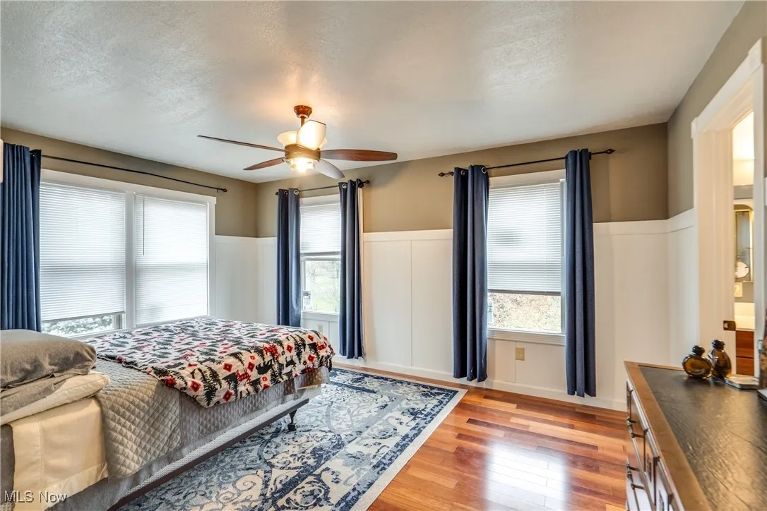 Bedroom with light wood finished floors, ceiling fan, a textured ceiling, and wainscoting