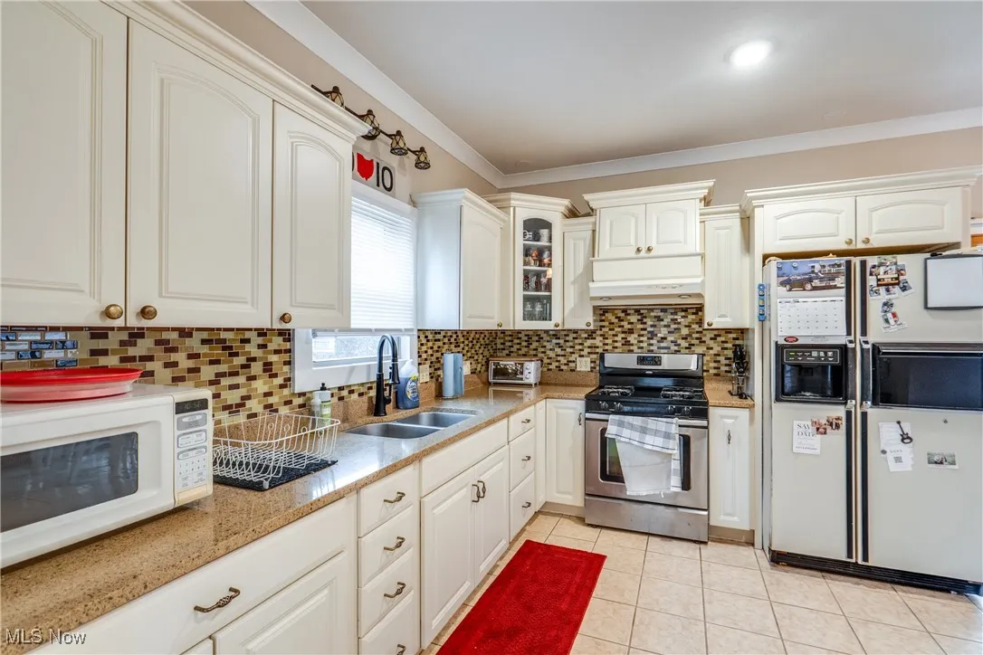 Kitchen with white appliances, tasteful backsplash, glass insert cabinets, light tile patterned flooring, and ornamental molding