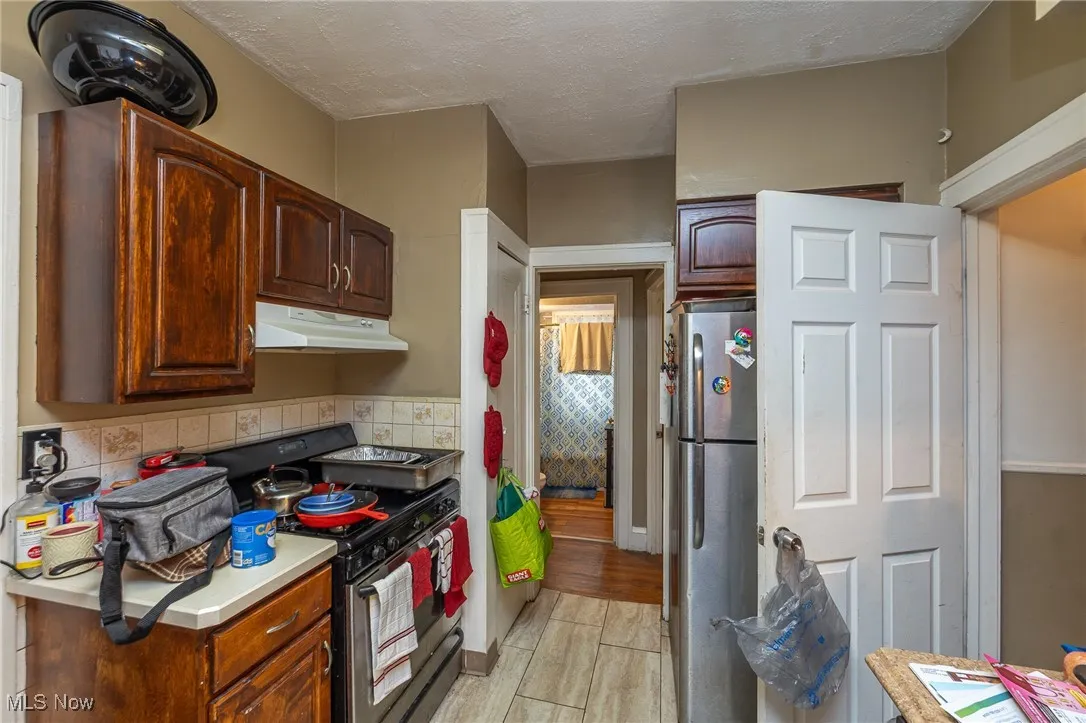 Kitchen with stainless steel appliances, light countertops, a textured ceiling, under cabinet range hood, and light wood-style floors