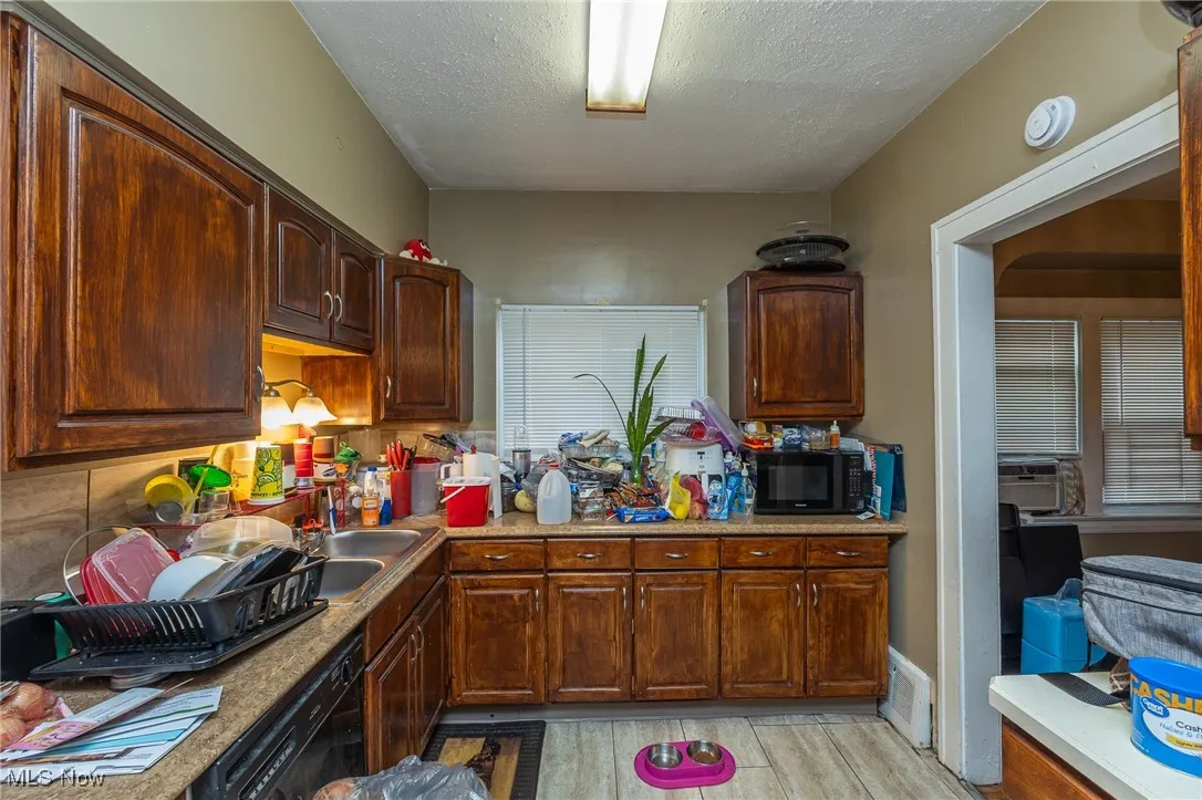 Kitchen with black appliances, a textured ceiling, light wood finished floors, and light countertops