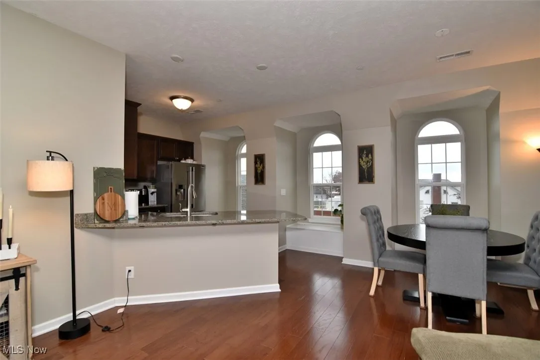 Kitchen featuring light stone countertops, dark wood finished floors, stainless steel refrigerator with ice dispenser, arched walkways, and a textured ceiling
