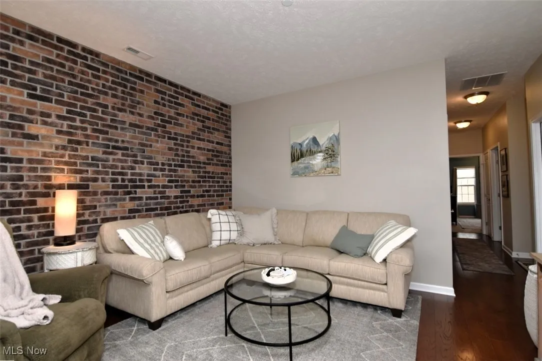 Living room featuring dark wood finished floors, brick wall, and a textured ceiling