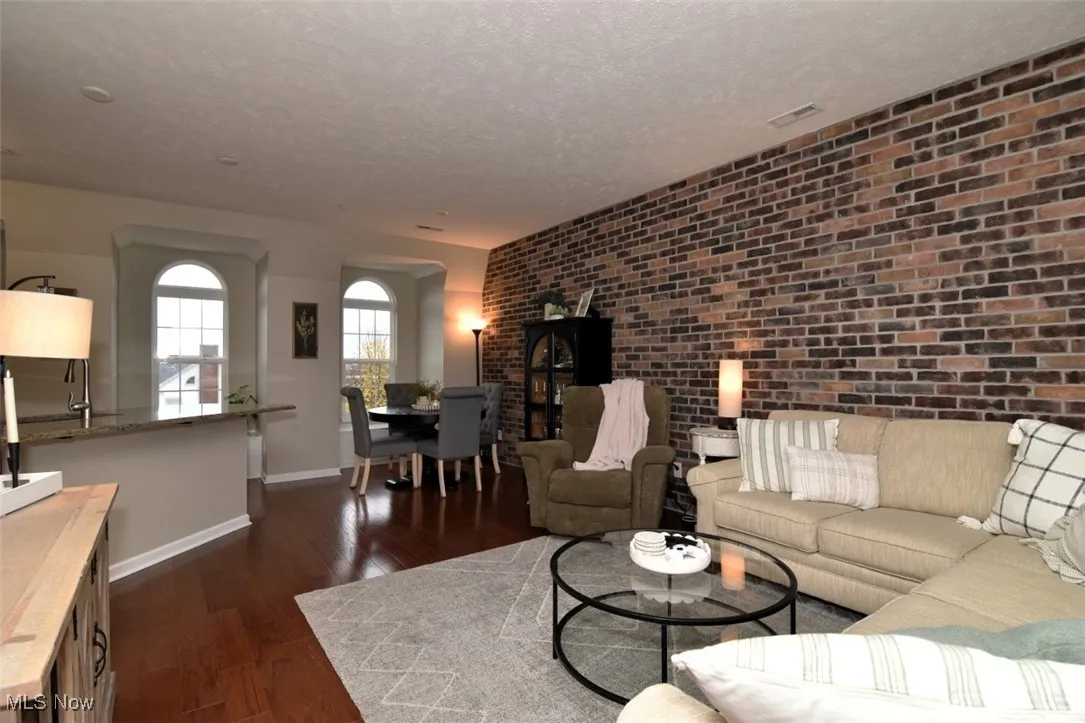 Living area featuring dark wood-type flooring, brick wall, and a textured ceiling