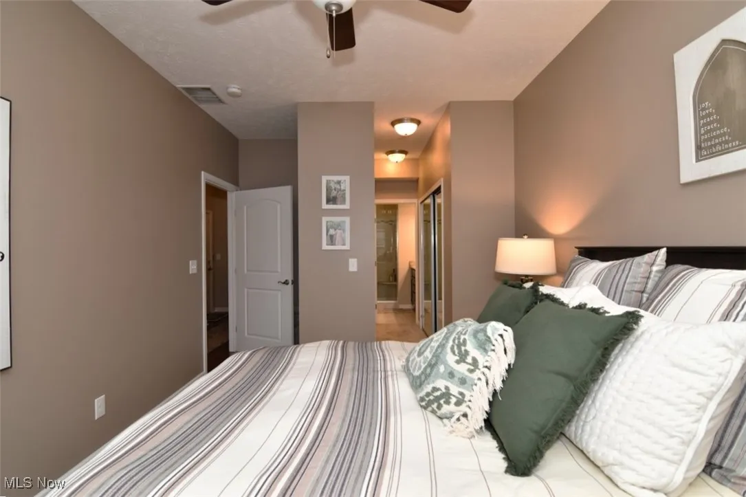 Bedroom with ensuite bathroom, a textured ceiling, a ceiling fan, and a closet