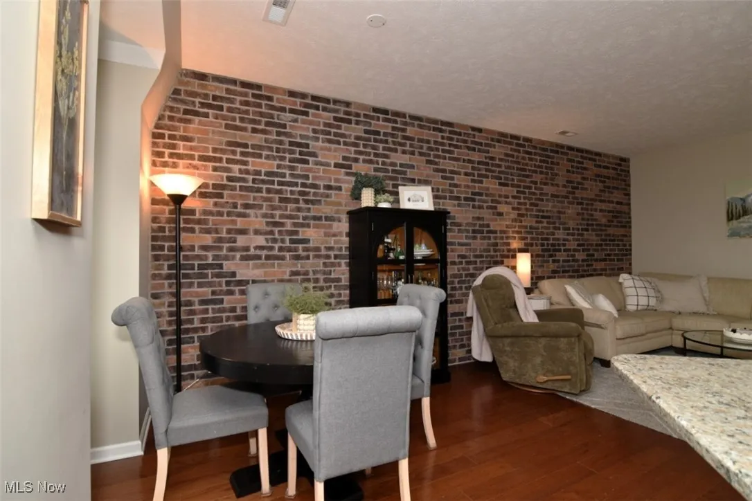 Dining space with dark wood-style flooring, brick wall, and a textured ceiling