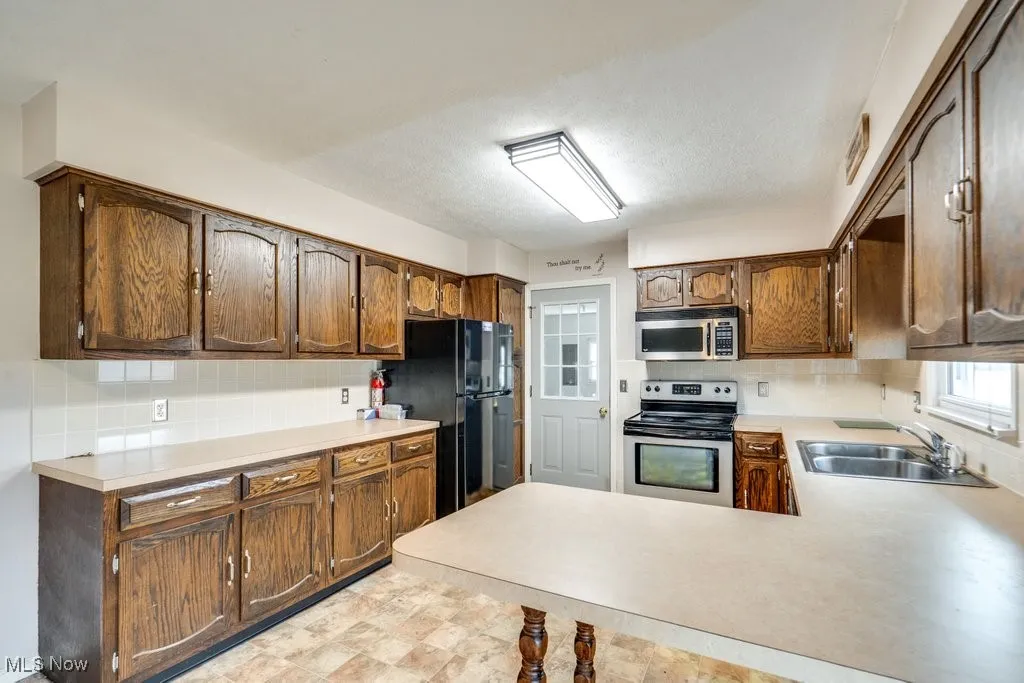Kitchen featuring tasteful backsplash, stainless steel appliances, light countertops, a textured ceiling, and a peninsula