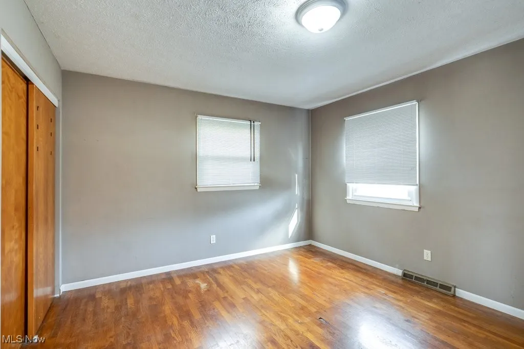 Unfurnished bedroom with a closet, wood finished floors, multiple windows, and a textured ceiling