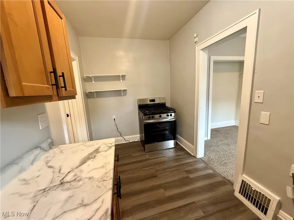 Kitchen featuring brown cabinets, stainless steel gas range oven, dark wood-style floors, light stone countertops, and open shelves