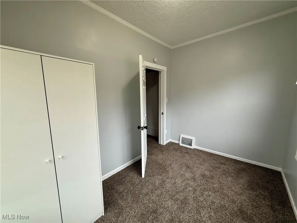 Unfurnished bedroom with dark colored carpet, ornamental molding, a textured ceiling, and a closet