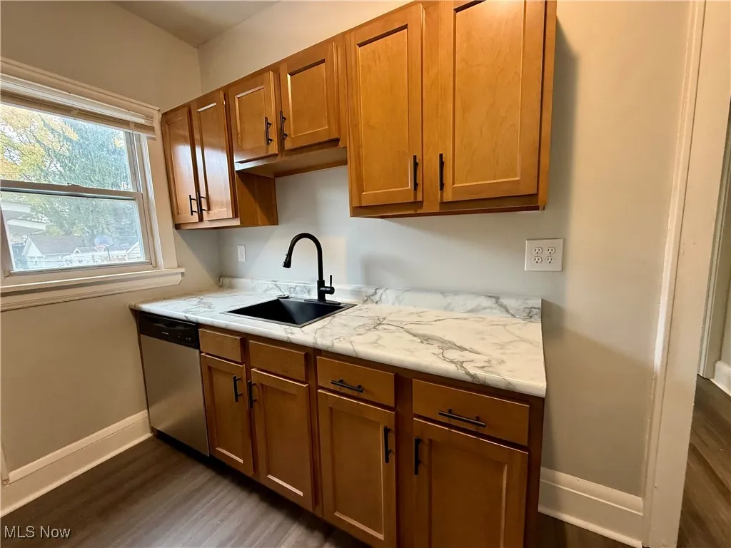Kitchen with brown cabinets, light countertops, stainless steel dishwasher, and dark wood-style flooring