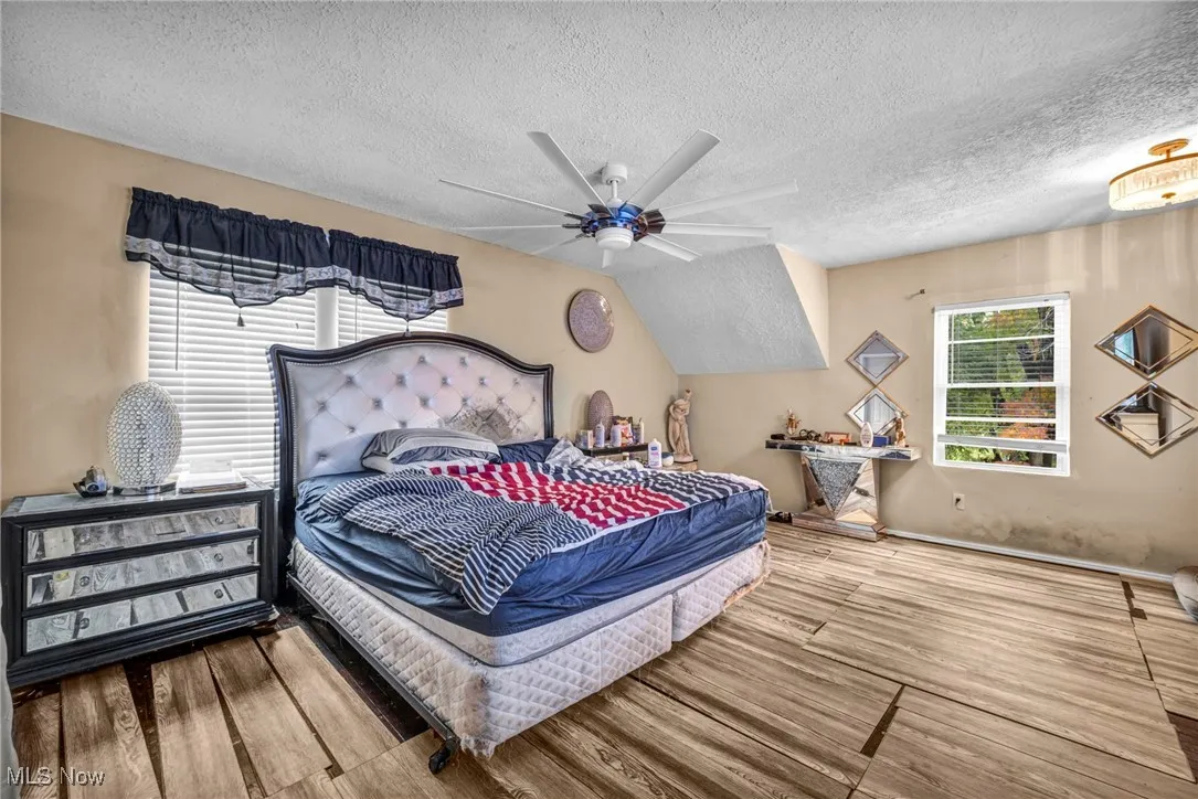 Bedroom with multiple windows, a textured ceiling, wood finished floors, and a ceiling fan