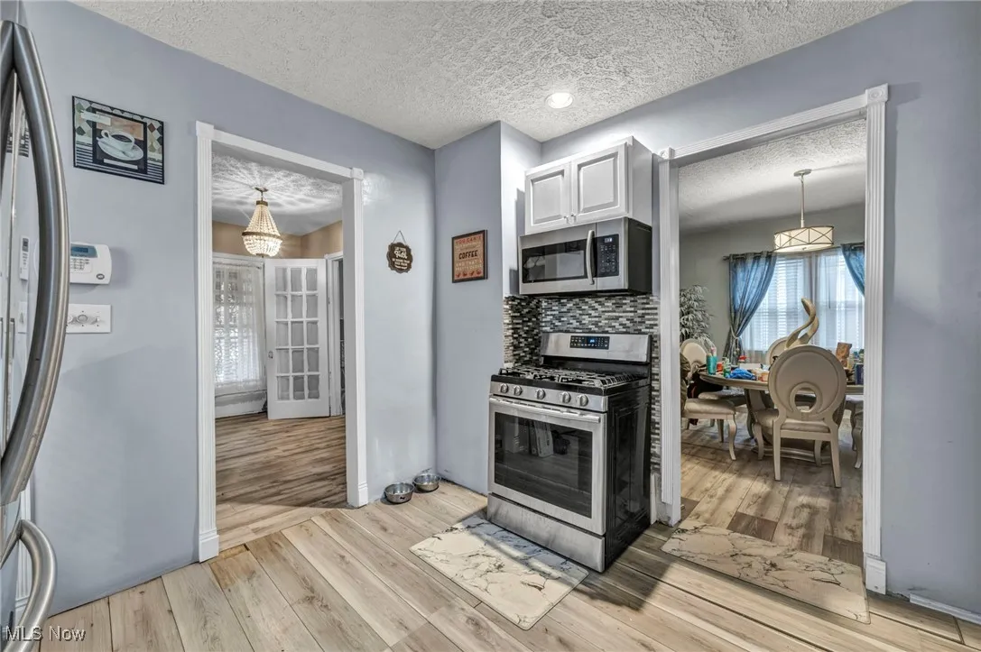 Kitchen with appliances with stainless steel finishes, a textured ceiling, backsplash, light wood-style floors, and white cabinetry