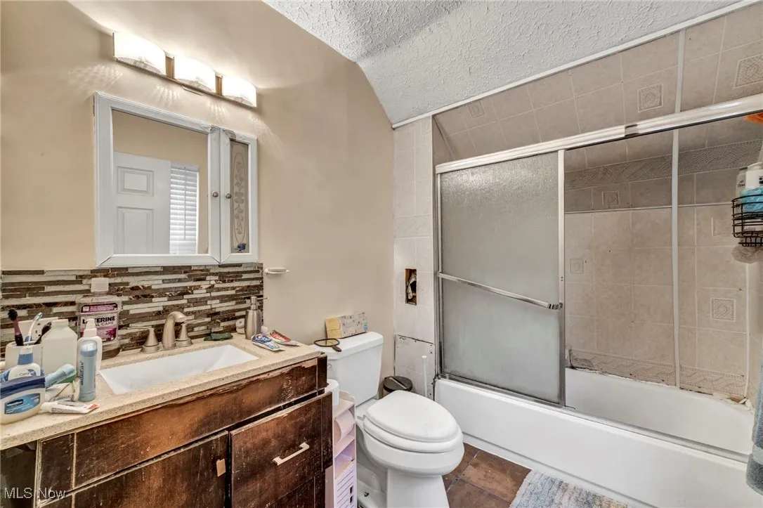 Bathroom with vanity, combined bath / shower with glass door, backsplash, a textured ceiling, and dark tile patterned floors