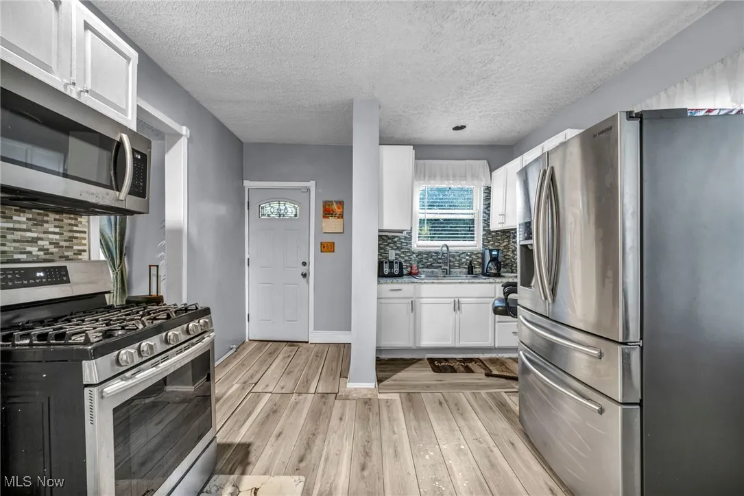 Kitchen with stainless steel appliances, white cabinetry, light wood-style floors, decorative backsplash, and a textured ceiling