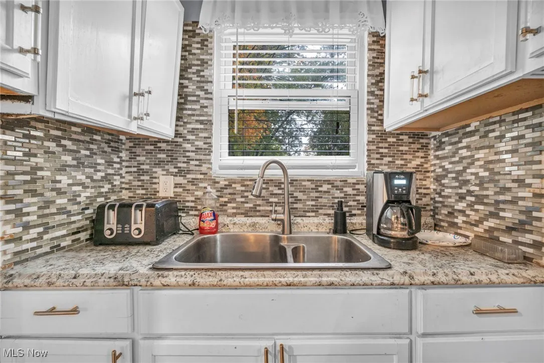 Kitchen with decorative backsplash, white cabinetry, and light stone countertops