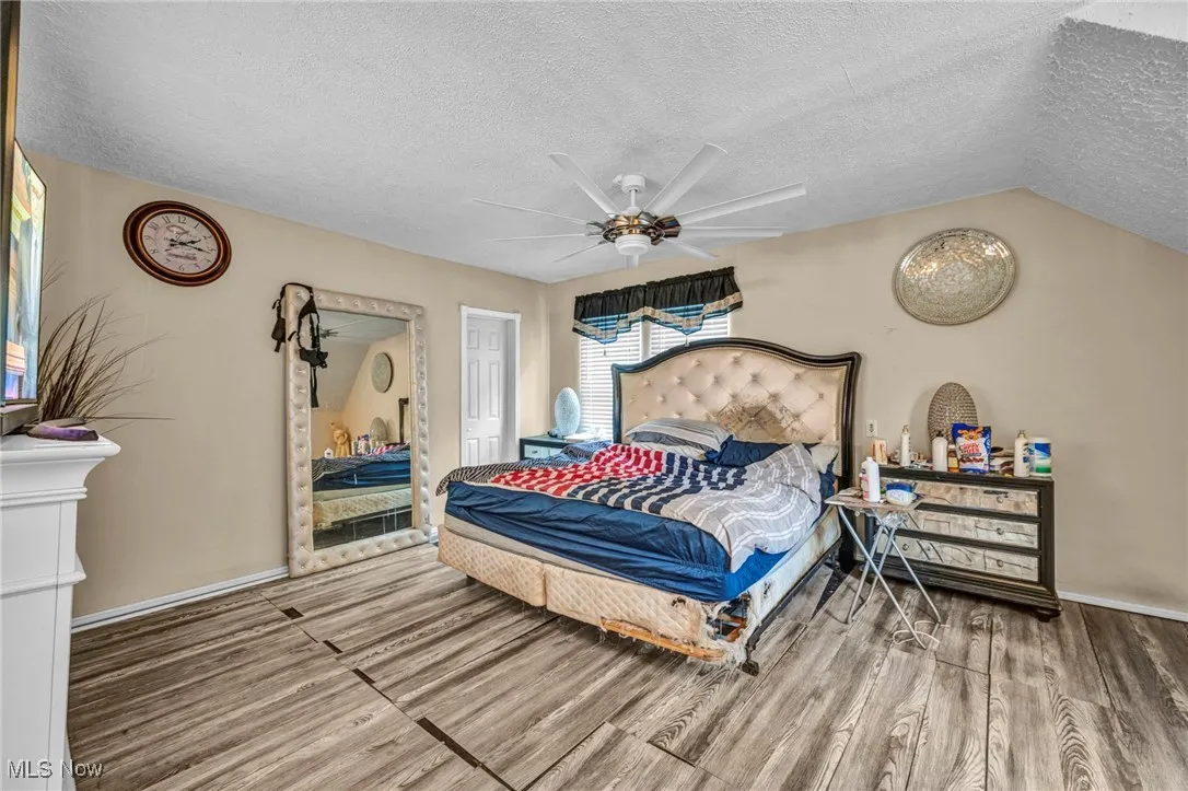 Bedroom with a textured ceiling, wood finished floors, ceiling fan, and lofted ceiling