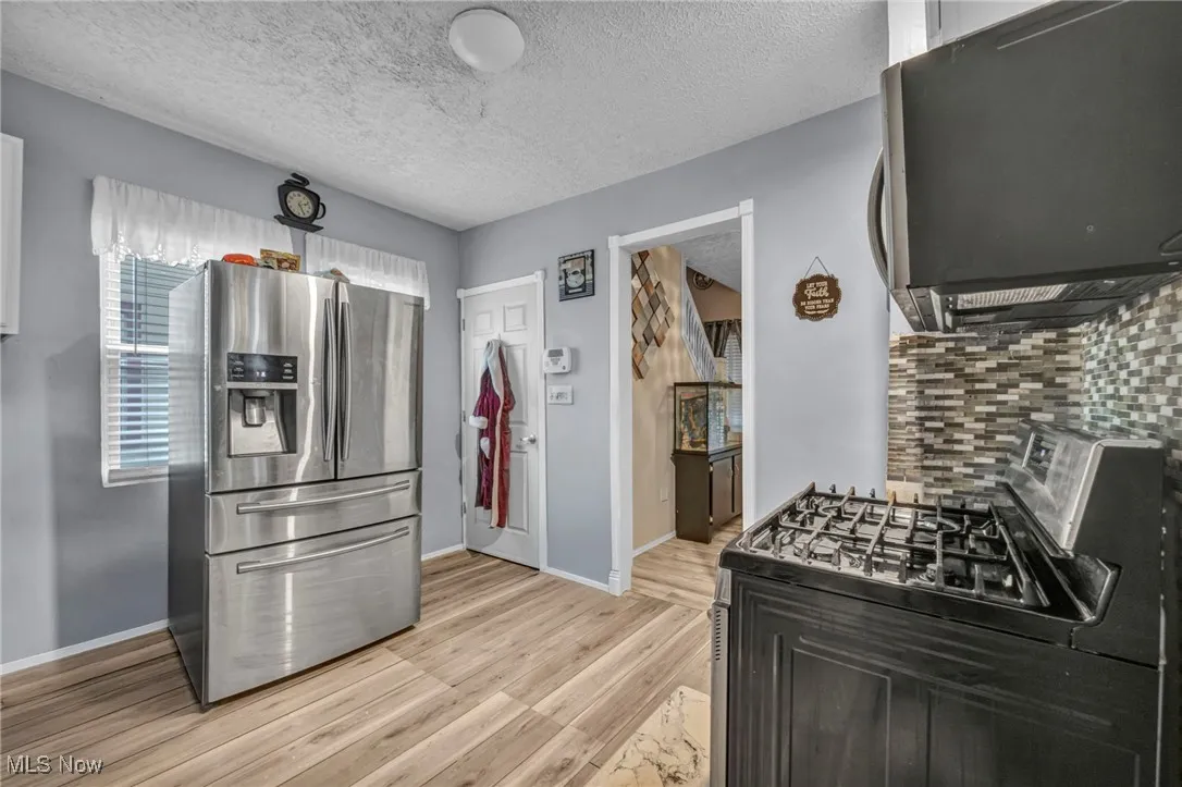 Kitchen with appliances with stainless steel finishes, a textured ceiling, light wood-style flooring, and tasteful backsplash