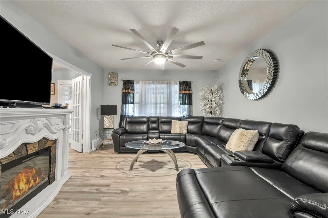 Living area featuring a glass covered fireplace, light wood-style flooring, a textured ceiling, and a ceiling fan