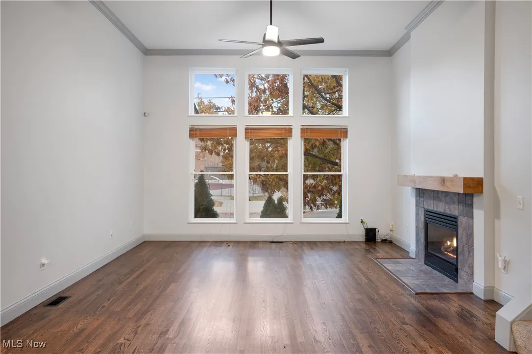 Unfurnished living room featuring crown molding, a fireplace, dark wood-type flooring, and ceiling fan
