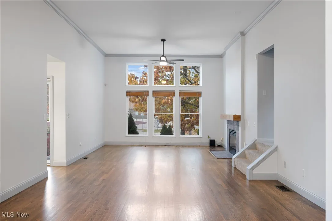 Unfurnished living room with crown molding, dark wood-style flooring, a fireplace, and ceiling fan