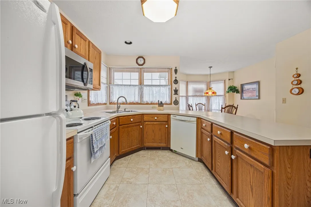 Kitchen featuring white appliances, brown cabinetry, light countertops, healthy amount of natural light, and recessed lighting