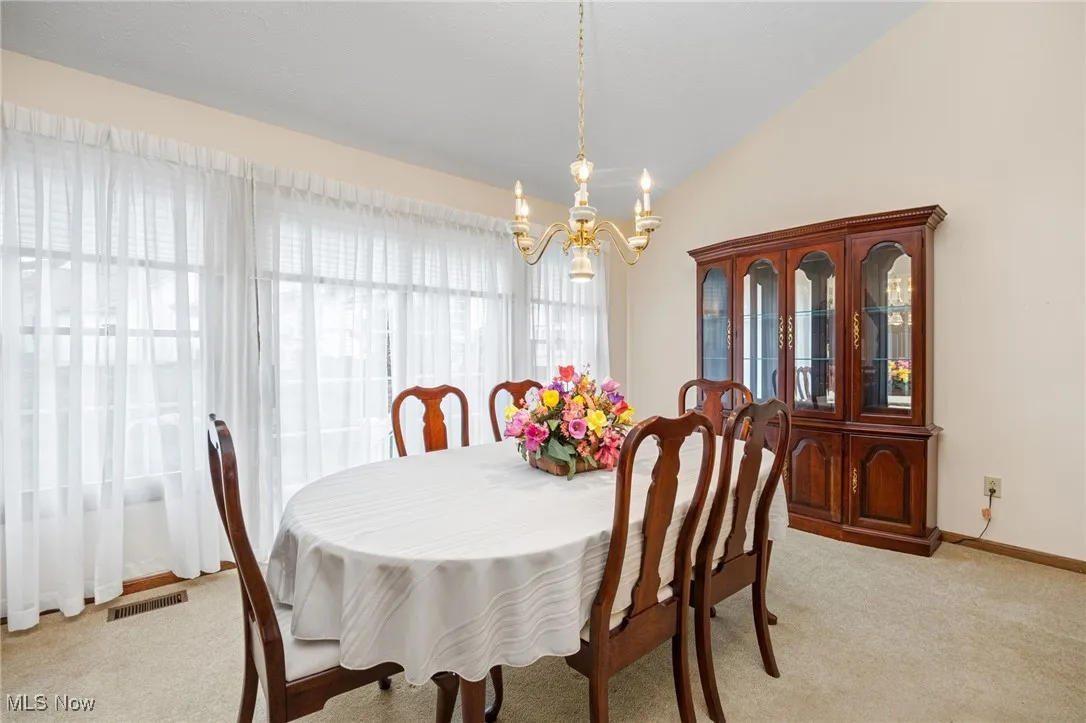 Dining room with lofted ceiling, light carpet, and a chandelier