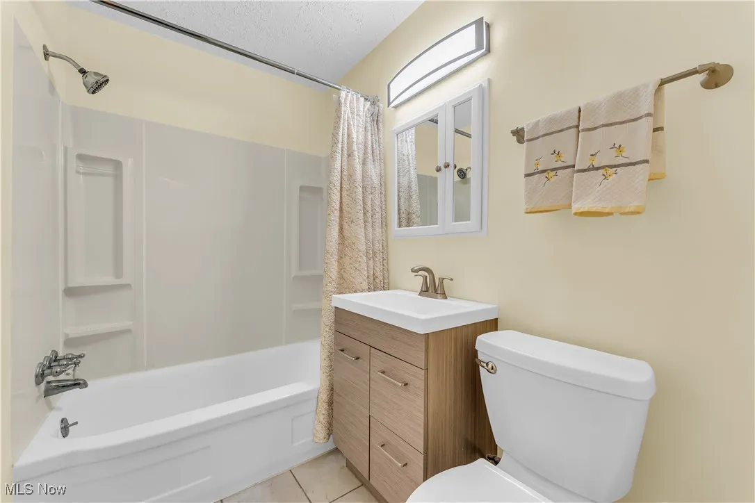 Full bathroom featuring vanity, shower / bathtub combination with curtain, a textured ceiling, and light tile patterned floors