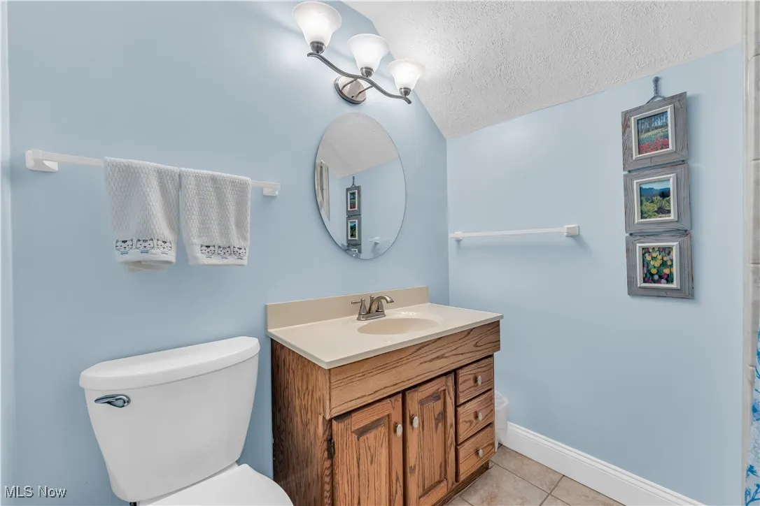 Bathroom featuring vanity, a textured ceiling, light tile patterned floors, a shower with shower curtain, and lofted ceiling
