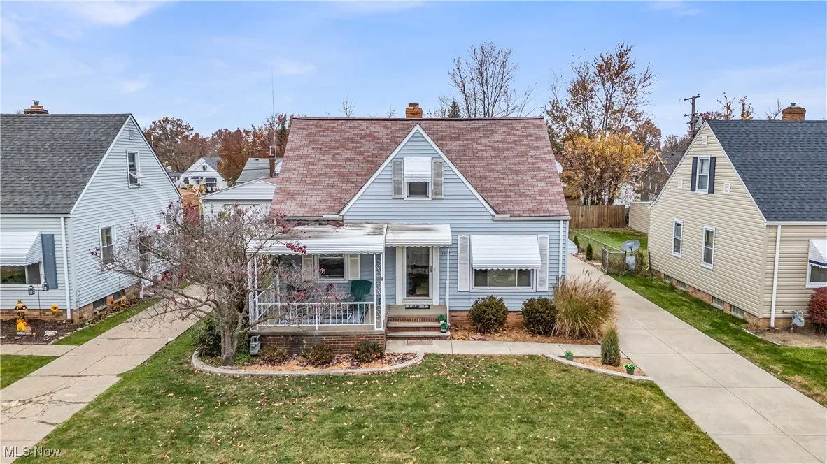 View of front of home with covered porch, a front yard, a chimney, and roof with shingles