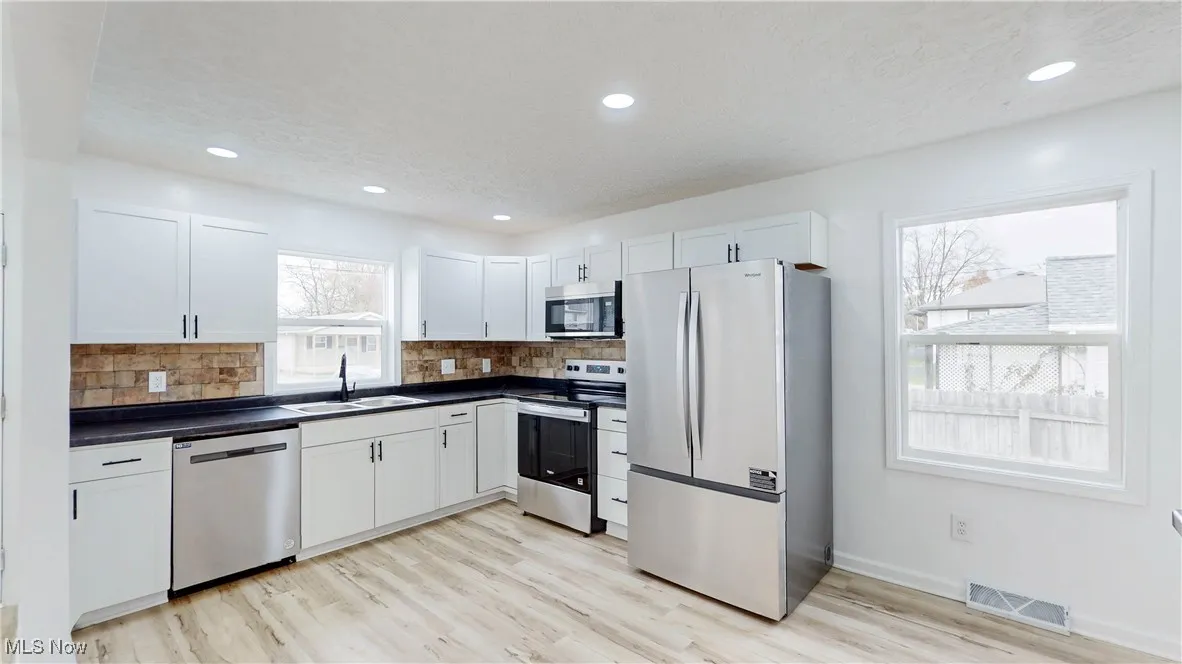 Kitchen featuring stainless steel appliances, white cabinetry, dark countertops, backsplash, and light wood finished floors