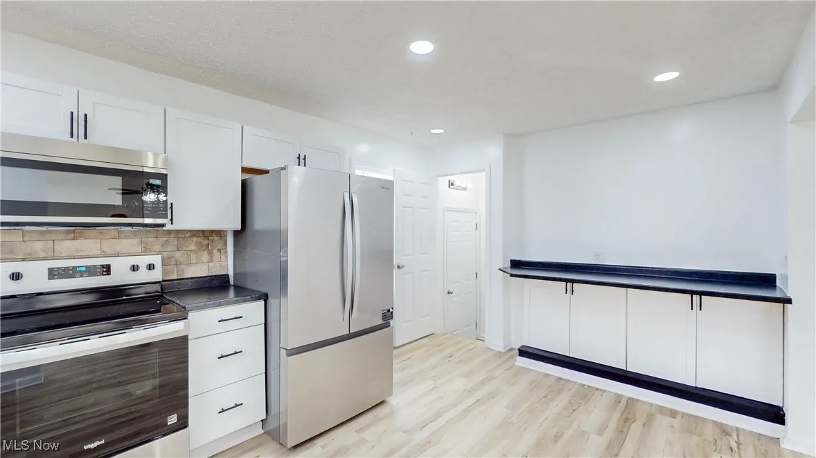 Kitchen featuring dark countertops, stainless steel appliances, decorative backsplash, white cabinetry, and recessed lighting
