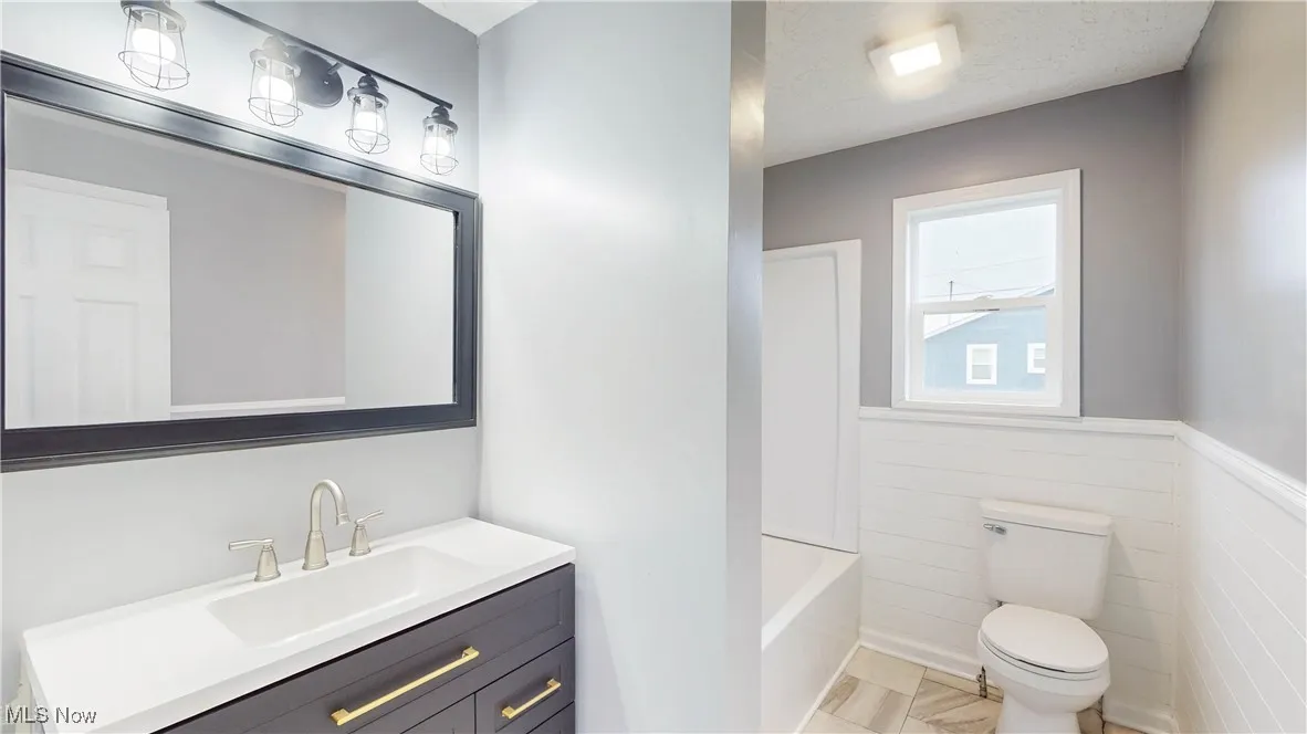 Full bathroom featuring a wainscoted wall, vanity, a textured ceiling, and bathing tub / shower combination