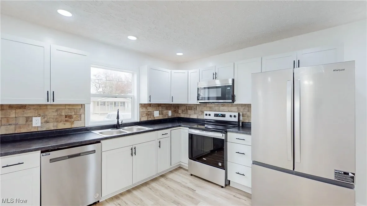 Kitchen with appliances with stainless steel finishes, dark countertops, white cabinetry, a textured ceiling, and light wood-type​​‌​​​​‌​​‌‌​‌‌​​​‌‌​‌​‌​‌​​​‌​​ flooring