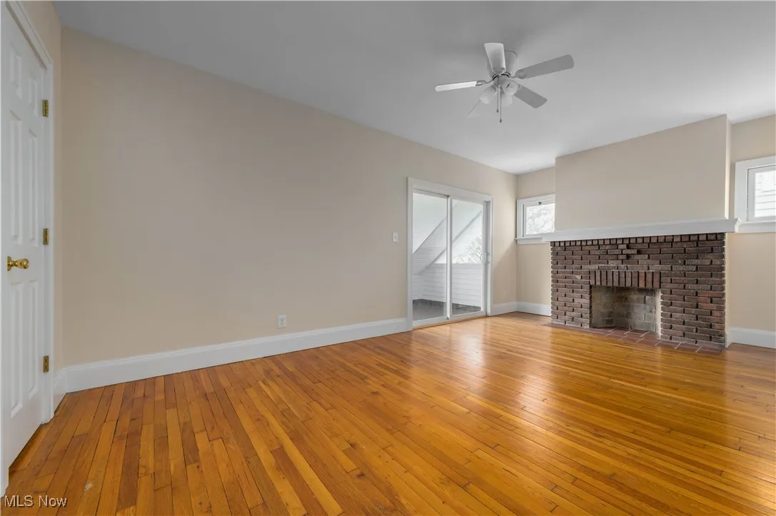 Unfurnished living room with a brick fireplace, light wood finished floors, and a ceiling fan