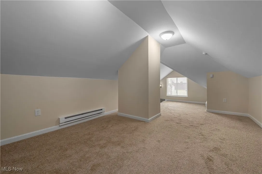 Bonus room with a baseboard radiator, light colored carpet, and vaulted ceiling