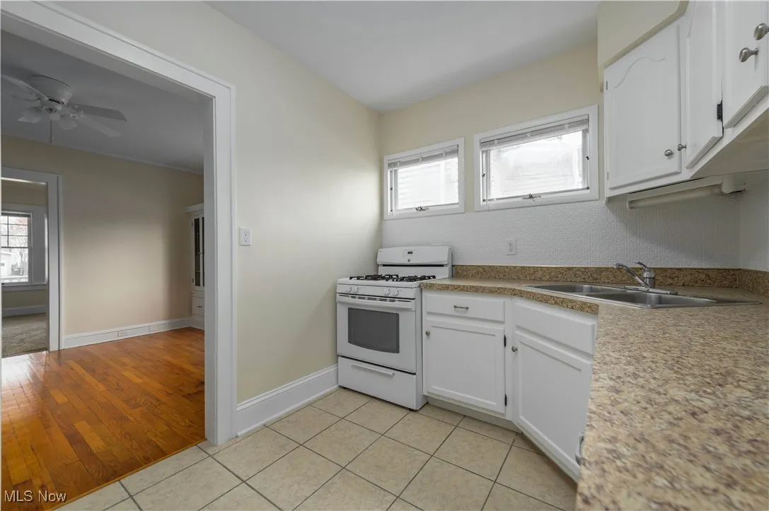 Kitchen with white range with gas cooktop, white cabinetry, light tile patterned floors, light countertops, and a ceiling fan