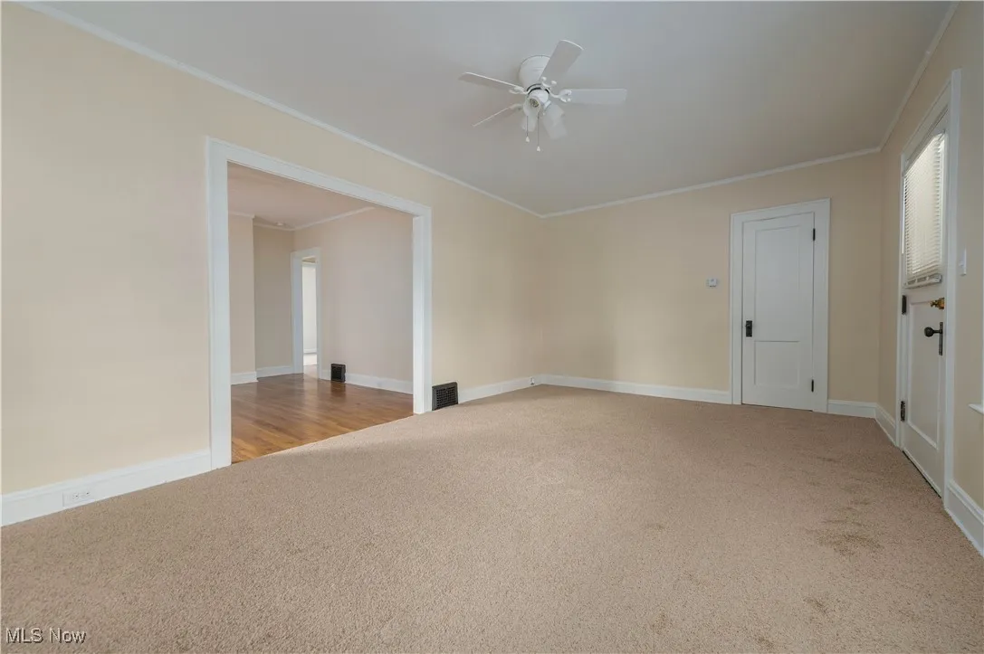 Spare room featuring light colored carpet, crown molding, and ceiling fan