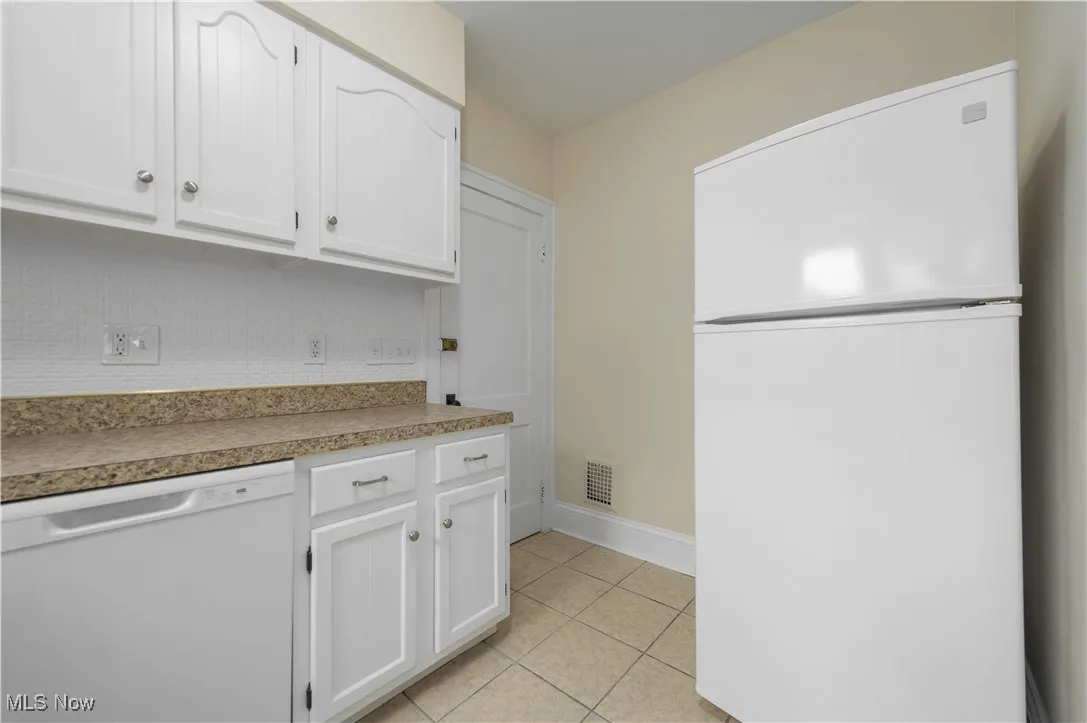 Kitchen featuring white appliances, white cabinets, light tile patterned flooring, and light countertops